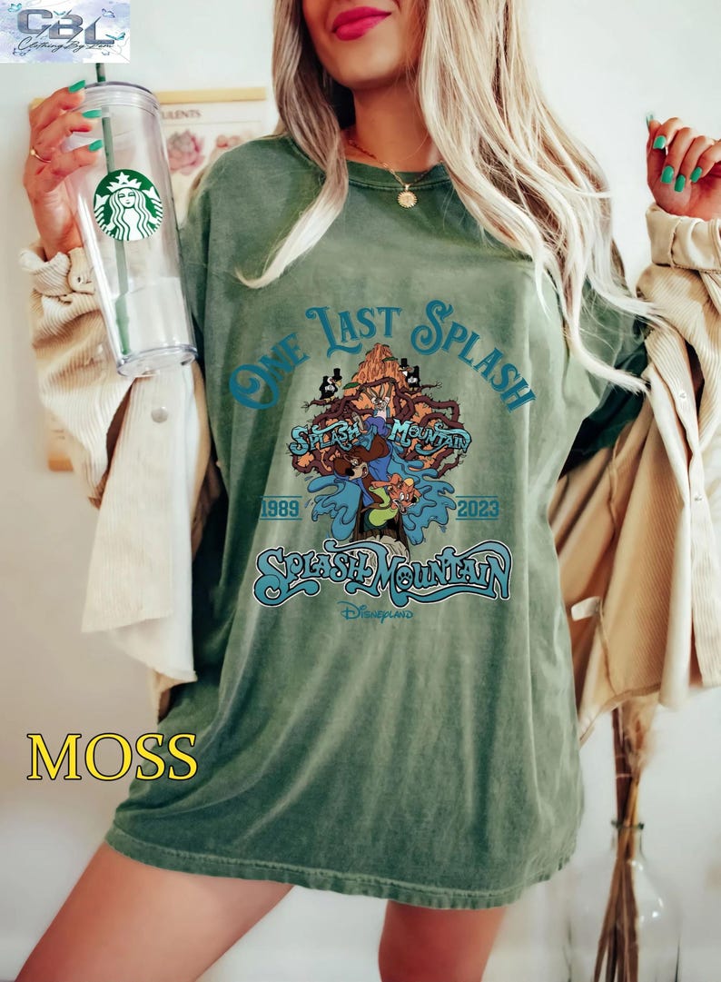 May include: Moss green t-shirt with the text "One Last Splash" and "Splash Mountain" in a teal font. The graphic features cartoon characters and the years 1989 and 2023. The shirt is a relaxed fit.