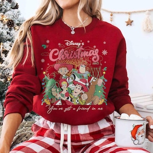 Może przedstawiać: Czerwona bluza z nadrukiem postaci z Toy Story Disneya, napisem "Disney's Christmas" i "You've got a friend in me". Bluza ma długie rękawy i okrągły dekolt.
