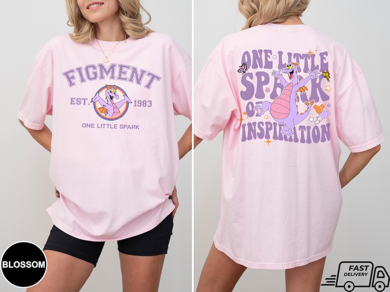 Op de afbeelding: Roze T-shirt met een paarse draak afbeelding en de tekst "Figment Est. 1983 One Little Spark" op de voorkant en "One Little Spark of Inspiration" op de achterkant.