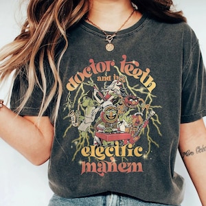 May include: Dark gray t-shirt featuring the Muppets' Electric Mayhem band. The design includes the band members playing instruments, with the text "Doctor Teeth and the Electric Mayhem" in a retro font, and lightning bolt graphics.