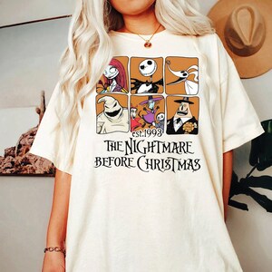 May include: Cream-colored t-shirt featuring a grid of six character illustrations from "The Nightmare Before Christmas" movie. The text "est.1993" and "THE NIGHTMARE BEFORE CHRISTMAS" are printed below the grid in black.