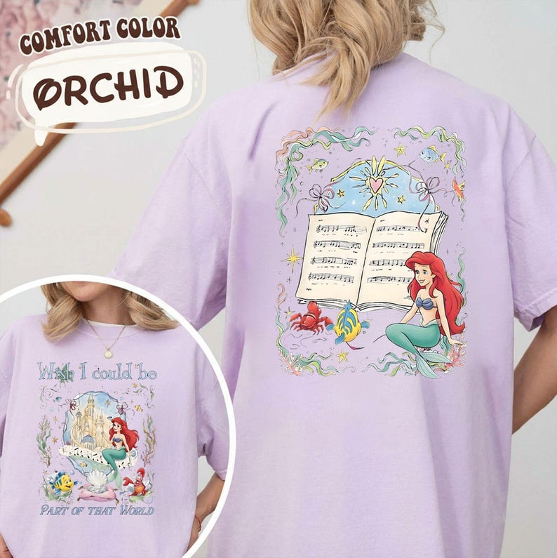 May include: Orchid-colored t-shirt featuring a graphic of Ariel from The Little Mermaid. The design includes a musical score, a crab, a fish, and Ariel. The shirt also has the text "Wish I could be Part of That World."
