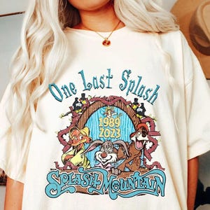 以下が含まれることがあります： クリーム色のTシャツ。カラフルなグラフィックで「One Last Splash」と「Splash Mountain」の文字が描かれています。グラフィックには漫画のキャラクターと1989年と2023年の年号が含まれています。半袖でゆったりとしたフィット感です。