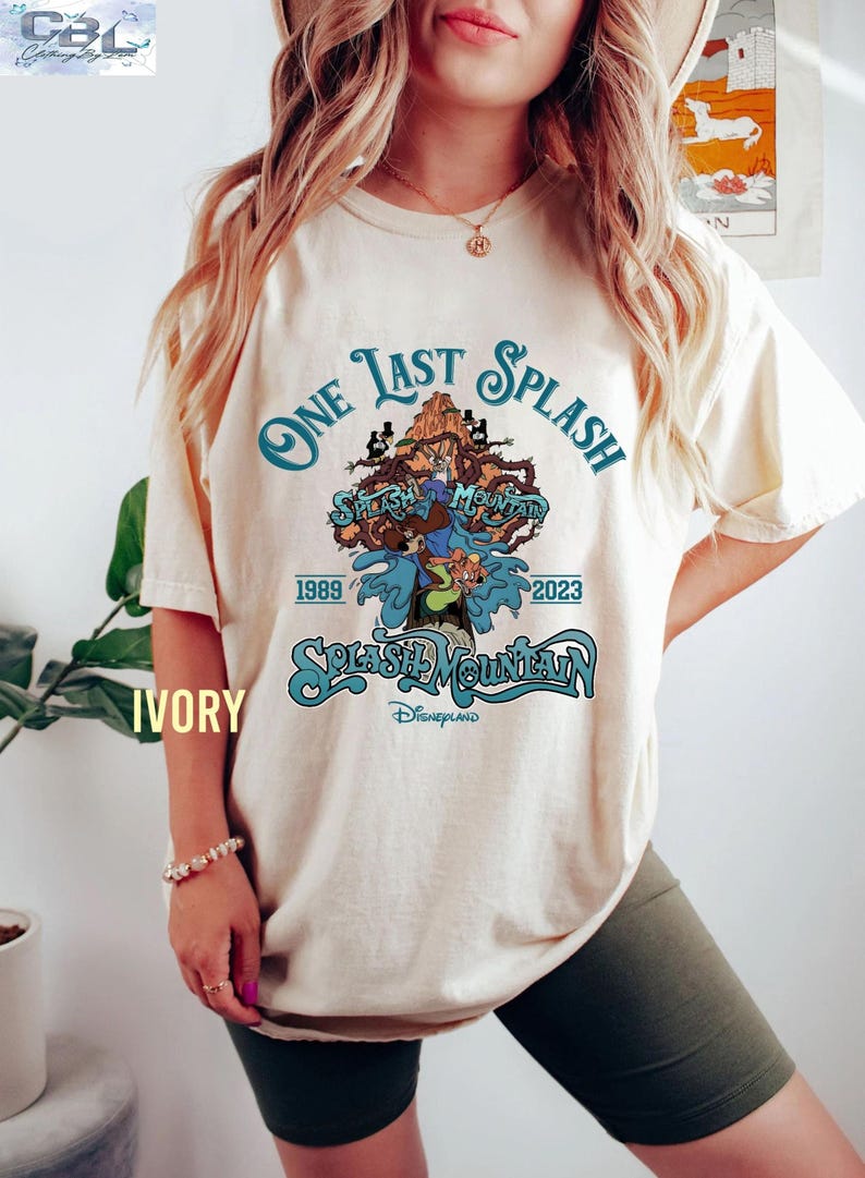 May include: Ivory-colored t-shirt featuring a graphic design for "Splash Mountain" at Disneyland. The design includes the text "One Last Splash" and the years 1989 and 2023, along with cartoon characters and a mountain scene.