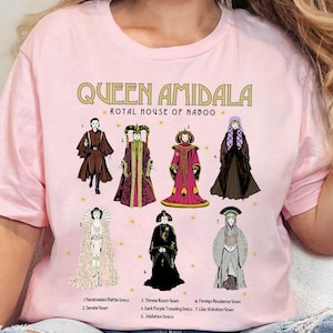 May include: Pink t-shirt with a graphic of Queen Amidala from Star Wars. The graphic shows different outfits worn by the character, including a handmaiden battle dress, senate gown, throne room gown, dark purple traveling dress, jubilation dress, foreign residence gown, and lilac visitation gown. The text "Queen Amidala Royal House of Naboo" is printed above the graphic.