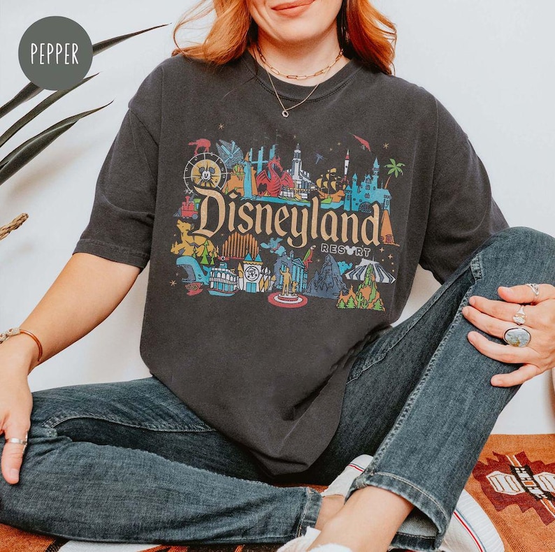 May include: A dark gray t-shirt with a colorful graphic of Disneyland park icons and the text "Disneyland Resort".