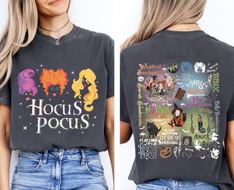 May include: Dark gray t-shirt featuring the text "Hocus Pocus" with illustrations of the Sanderson sisters' hair and a variety of themed graphics on the back. The shirt is a comfortable, casual style.