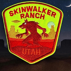 May include: A shield-shaped embroidered patch with a bright yellow background and a red border. It features the red text SKINWALKER RANCH and UTAH. A red creature stands in the center against a desert landscape with a flying saucer and a moon.