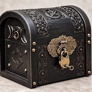 May include: A black wooden chest with a domed lid featuring a pentagram emblem, a triple moon symbol on the side, and ornate brass-toned metal hardware. The front includes a decorative latch secured with a small brass padlock and a matching key.