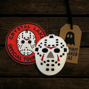 May include: Two patches and a tag are displayed. One patch is round with a red border and the words "CRYSTAL LAKE OFFICIAL TOUR" around a white hockey mask. The other patch is a white hockey mask. A brown tag with a ghost graphic and the words "SPIRIT SEEKER AZ" hangs from the top.