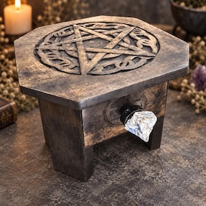 May include: A small, dark brown wooden box with a hexagonal top featuring a carved pentagram design. The box stands on four short legs and includes a single drawer front adorned with a clear, rough-cut crystal knob that serves as a handle.