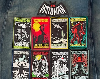 May include: A collection of nine embroidered patches on denim fabric. One bat-shaped patch reads MOTHMAN. Eight rectangular patches feature cryptozoology themes including Loch Ness Monster, Jackalope, Extraterrestrials, Sasquatch, Chupacabra, Jersey Devil, Mothman, and Flatwoods Monster.
