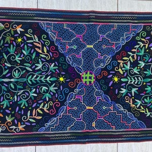 May include: Embroidered textile with a dark background and colorful floral and geometric patterns. The design features a central diamond shape with intricate details, surrounded by leaves and flowers in shades of green, orange, and pink.