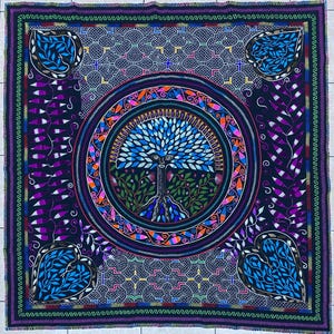 May include: A square, intricately designed textile featuring a central tree of life motif in blue and green, surrounded by a circular border with colorful accents. The corners have heart-shaped designs with blue leaves, all set against a dark background.