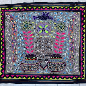 May include: A vibrantly colored textile with a black background, featuring a central design of two pots and a central figure. The border is a zigzag pattern in pink and yellow. The design includes a bird, leaves, and floral elements in various colors.