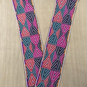 May include: Two colorful woven textile strips with geometric patterns in red, pink, teal, and black. The edges are trimmed with white and yellow, and the ends have purple fringe. The design features repeating triangles and diamond shapes.