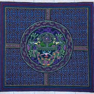 May include: A square textile with a complex geometric design in shades of blue, purple, green, and red. The central motif is a circular design featuring a face and two frogs. The border has a repeating pattern.
