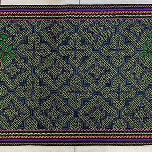 May include: A woven tapestry with a repeating geometric pattern in shades of green, blue, and black. Two stylized frogs with yellow spots are on either side of the pattern, surrounded by green leaves and pink flowers.