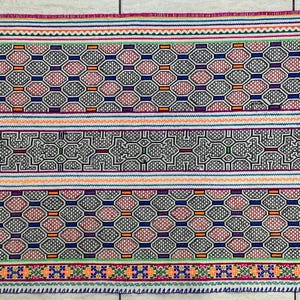 May include: A colorful woven rug with a geometric pattern in shades of pink, blue, green, orange, and white. The rug has a repeating pattern of hexagons and squares.