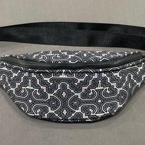 May include: A black fanny pack with a geometric pattern in white, black, and pink. The bag has a zipper closure and an adjustable strap.
