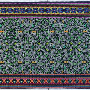 May include: A rectangular textile with a complex, symmetrical pattern. The central design is primarily gray and green, with accents of yellow and orange. Borders feature bands of blue, purple, and red with intricate geometric details. The textile is likely hand-woven.