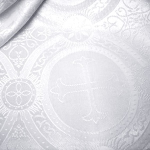 May include: White fabric with a raised, embossed pattern of repeating crosses and floral designs. The fabric has a subtle sheen and a smooth texture.