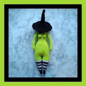 May include: A handmade crochet witch doll with a black hat and a lime green body. The doll has black and white striped socks and black shoes. The witch doll is displayed against a marble background.