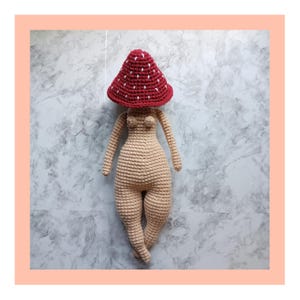 May include: A crocheted doll with a red and white mushroom hat. The doll is nude and has a simple, minimalist design.