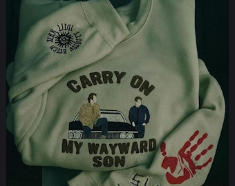 Op de afbeelding: Een lichtbeige sweater met ronde hals en een geborduurde afbeelding van twee figuren bij een zwarte auto met de tekst CARRY ON MY WAYWARD SON. De mouw toont een rode handafdruk en symbolen, bij de kraag bevindt zich een cirkelvormig embleem.