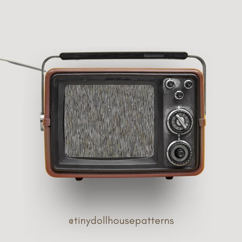 Op de afbeelding: Een vintage-stijl, bruin en zwarte televisie met een statisch scherm. De televisie heeft een zilveren knop en een zilveren handvat aan de bovenkant.
