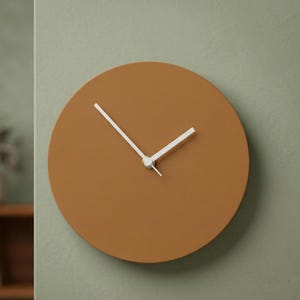 May include: A circular wall clock with a solid matte terracotta brown face and two simple white hands. The clock features a clean, frameless design with no numbers or markings on the dial, centered around a small silver-toned central hub.