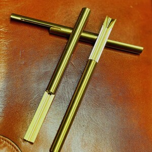 以下が含まれることがあります： 黒いハンドルと「But First, Coffee」のテキストが黒い太字で書かれた白いセラミックマグ。マグは白い表面に置かれています。