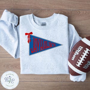 May include: A light gray sweatshirt with a blue pennant that reads "JAYHAWKS" in red lettering. A red bow is attached to the pennant. A brown and white football is on the right side of the sweatshirt.