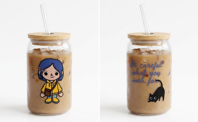 May include: Glass tumbler with a bamboo lid and straw, filled with iced coffee. One tumbler features a cartoon character in a yellow jacket. The other tumbler has the text "Be careful what you wish for" and a black cat.