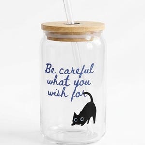 May include: A clear glass tumbler with a wooden lid and a clear straw. The tumbler features the text "Be careful what you wish for" in blue script, and a black cat illustration.