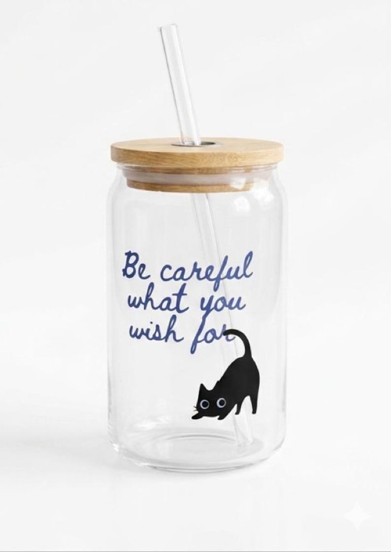May include: A clear glass tumbler with a wooden lid and a clear straw. The tumbler features the text "Be careful what you wish for" in blue script, and a black cat illustration.