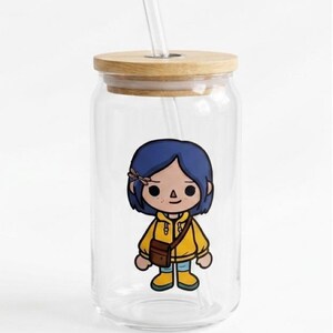 May include: A clear glass tumbler with a wooden lid and a clear straw. The tumbler features a cartoon illustration of a character with blue hair, a yellow jacket, and a brown bag. The tumbler is designed for cold drinks.