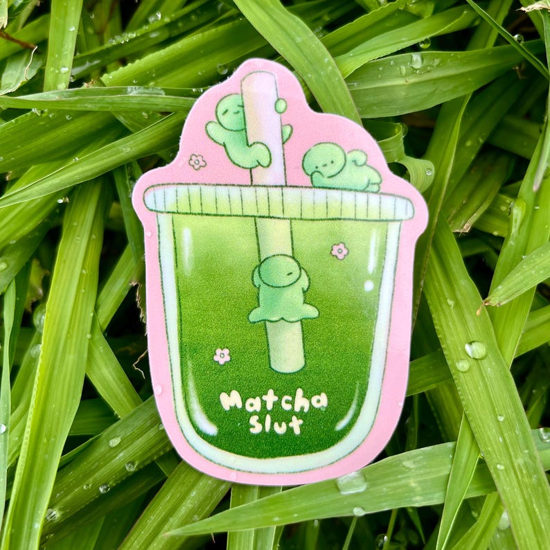 May include: A pink-edged sticker depicting a green matcha drink with a straw and three small green figures. The text "Matcha Slut" is at the bottom. Small pink flowers decorate the sticker.