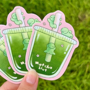 May include: Three stickers with a cartoon matcha drink design. The stickers have a pink border and the text "Matcha Slut". The drink is green with a straw and cute green characters.