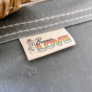 May include: A white fabric label with the text "Beanie LOVE" in rainbow letters and a peace sign with a heart above it.