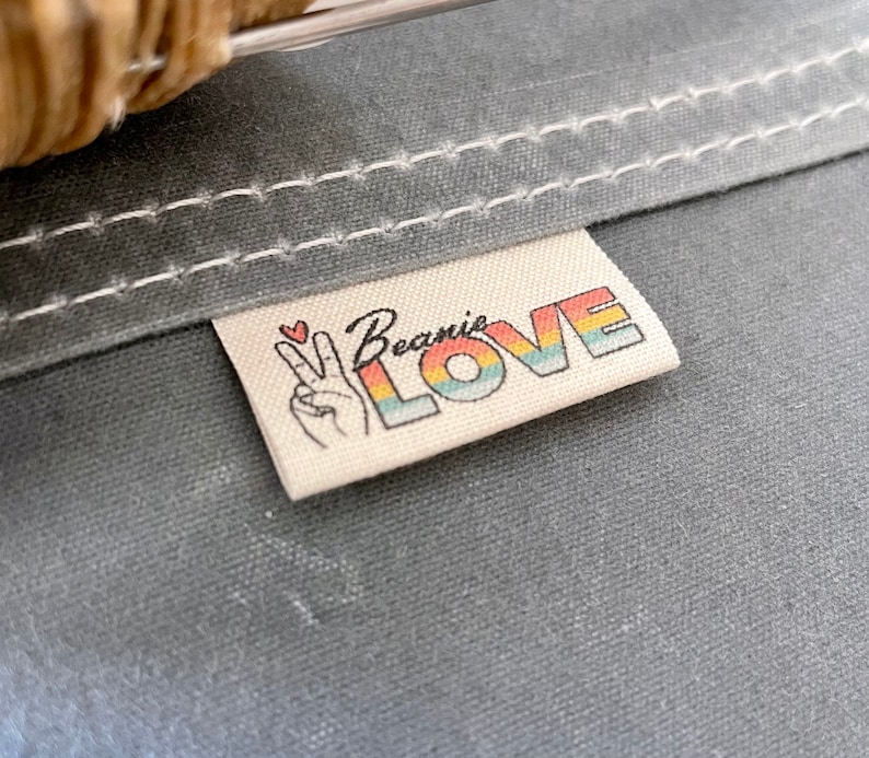 May include: A white fabric label with the text "Beanie LOVE" in rainbow letters and a peace sign with a heart above it.