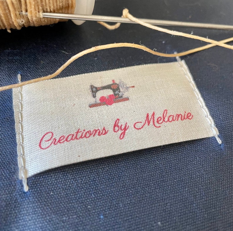 May include: A white fabric label with red text that reads "Creations by Melanie". A small black and white illustration of a sewing machine is above the text.