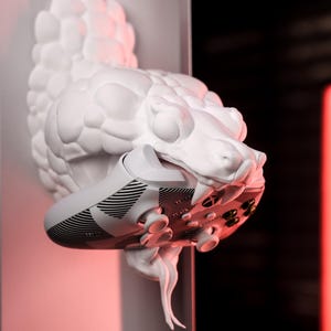 May include: A white, textured, snake-like sculpture with a white athletic shoe in its mouth. The shoe has black and white stripes and a black sole.