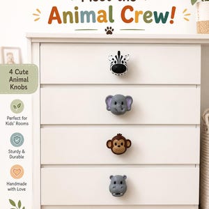 Può includere: Quattro pomelli per cassetti a forma di teste di animali, tra cui una zebra bianca e nera, un elefante grigio, una scimmia marrone e un ippopotamo grigio. I pomelli sono fissati su una cassettiera bianca a quattro cassetti. Il testo recita Meet the Animal Crew!