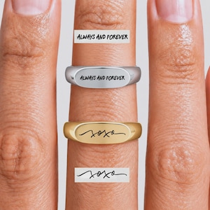 Könnte beinhalten: Zwei Siegelringe mit individuellen Gravuren. Der obere silberfarbene Ring ist mit dem Text ALWAYS AND FOREVER graviert. Der untere goldfarbene Ring trägt die kursive Gravur xoxo. Beide Ringe haben eine glatte, polierte Oberfläche.