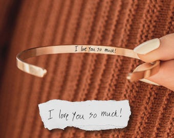 May include: A rose gold-toned metal cuff bracelet featuring the engraved black text I love You so much! on the inner surface. Below the bracelet, a torn piece of white paper displays the same handwritten phrase I love You so much! in black ink.