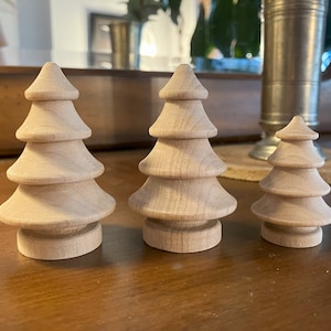 May include: Three wooden Christmas tree ornaments in different sizes. The trees are made of natural wood and have a simple, rustic design.