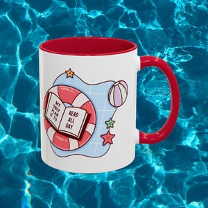 Pode incluir: Uma caneca de cerâmica branca com interior e alça vermelhos, apresentando um gráfico de uma boia de piscina com listras rosas e brancas, uma bola de praia, duas estrelas-do-mar e um livro aberto com o texto MY ONLY PLAN IS TO READ ALL DAY.