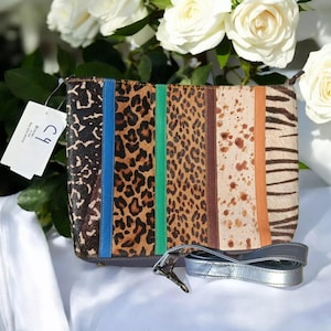 May include: A multi-colored animal print clutch bag with a silver strap. The bag has a brown, black, white, and tan animal print design with blue and green stripes. The bag has a tag that says "CJ"