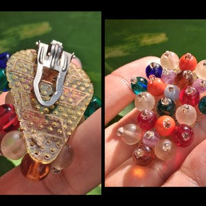 Puede incluir: Pendientes vintage de clip con un respaldo de filigrana dorada y un clip plateado. Los pendientes presentan un grupo de cuentas coloridas en tonos rojos, azules, verdes, naranjas y transparentes. Las cuentas son redondas y brillantes.